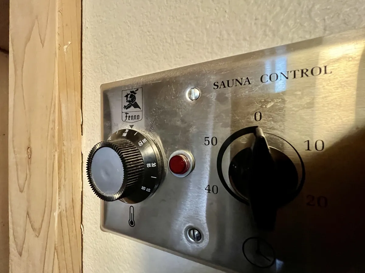 A detailed view of the sauna’s control panel, thermometer, and dial knobs. The focus on these functional elements underscores the personalized and luxurious experience of preparing for a sauna session.