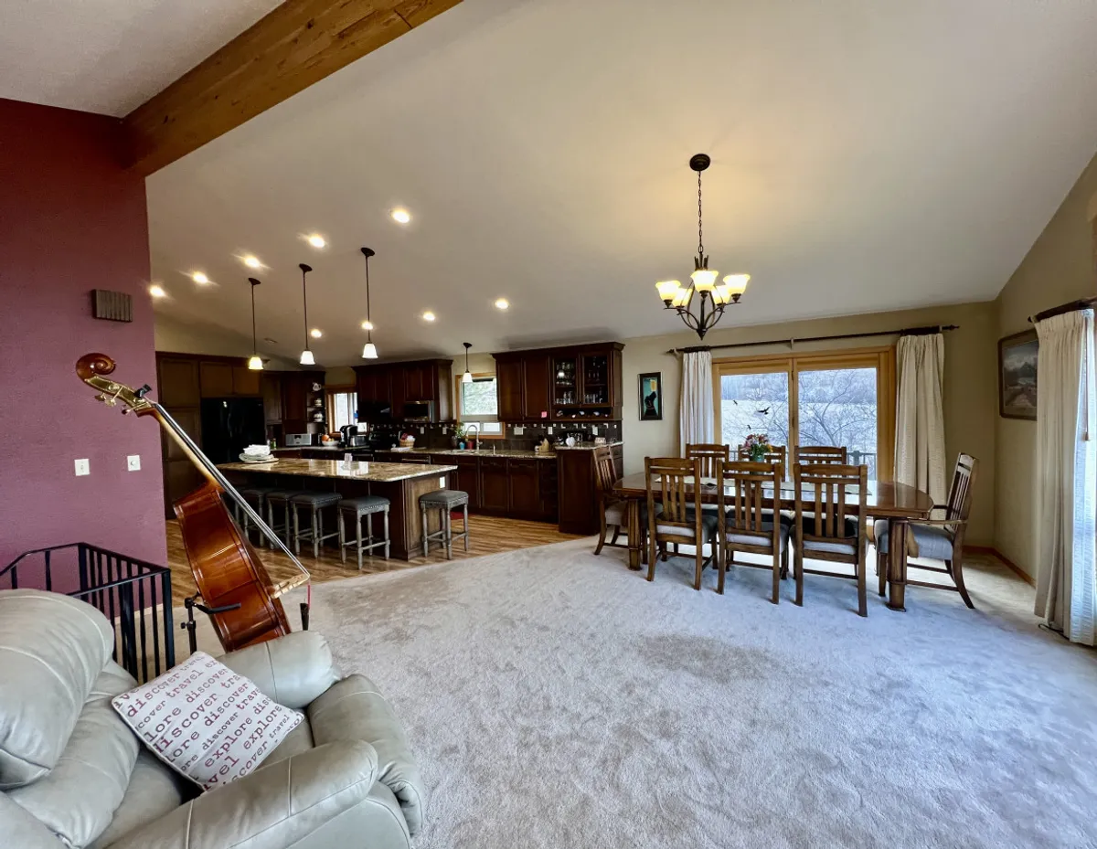 An open-concept living and dining area seamlessly flows into a modern kitchen, with a kitchen island, dining table, and comfortable sofa all within the same sightline. The presence of a double bass hints at musical or playful moments, and the space radiates warmth and togetherness.