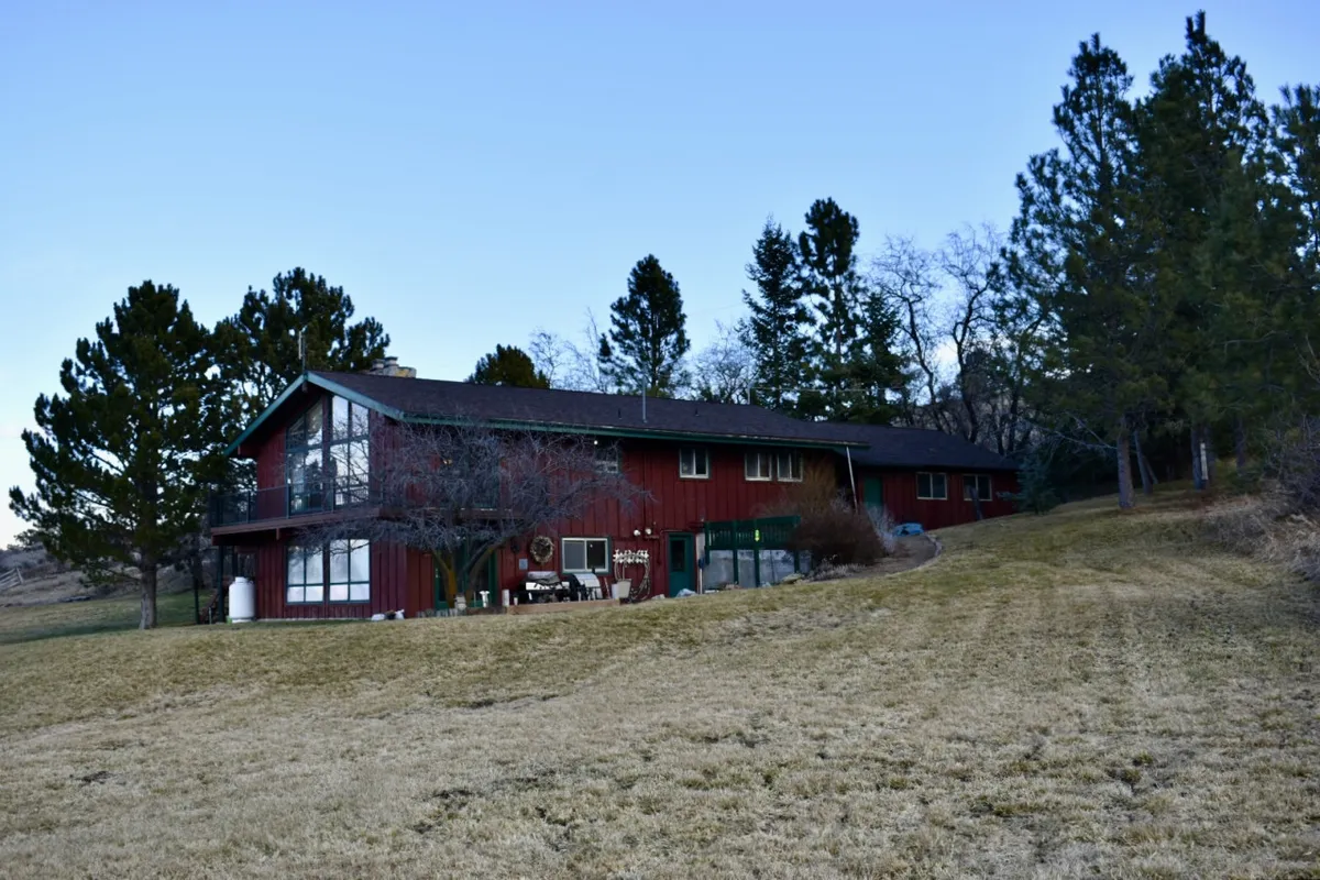This image features a red wooden house surrounded by green and brown trees and an expansive grassy area, offering a clear sense of space and natural beauty. The lush lawn is ideal for outdoor activities, gatherings, and play, and the setting evokes a peaceful, family-friendly vibe.