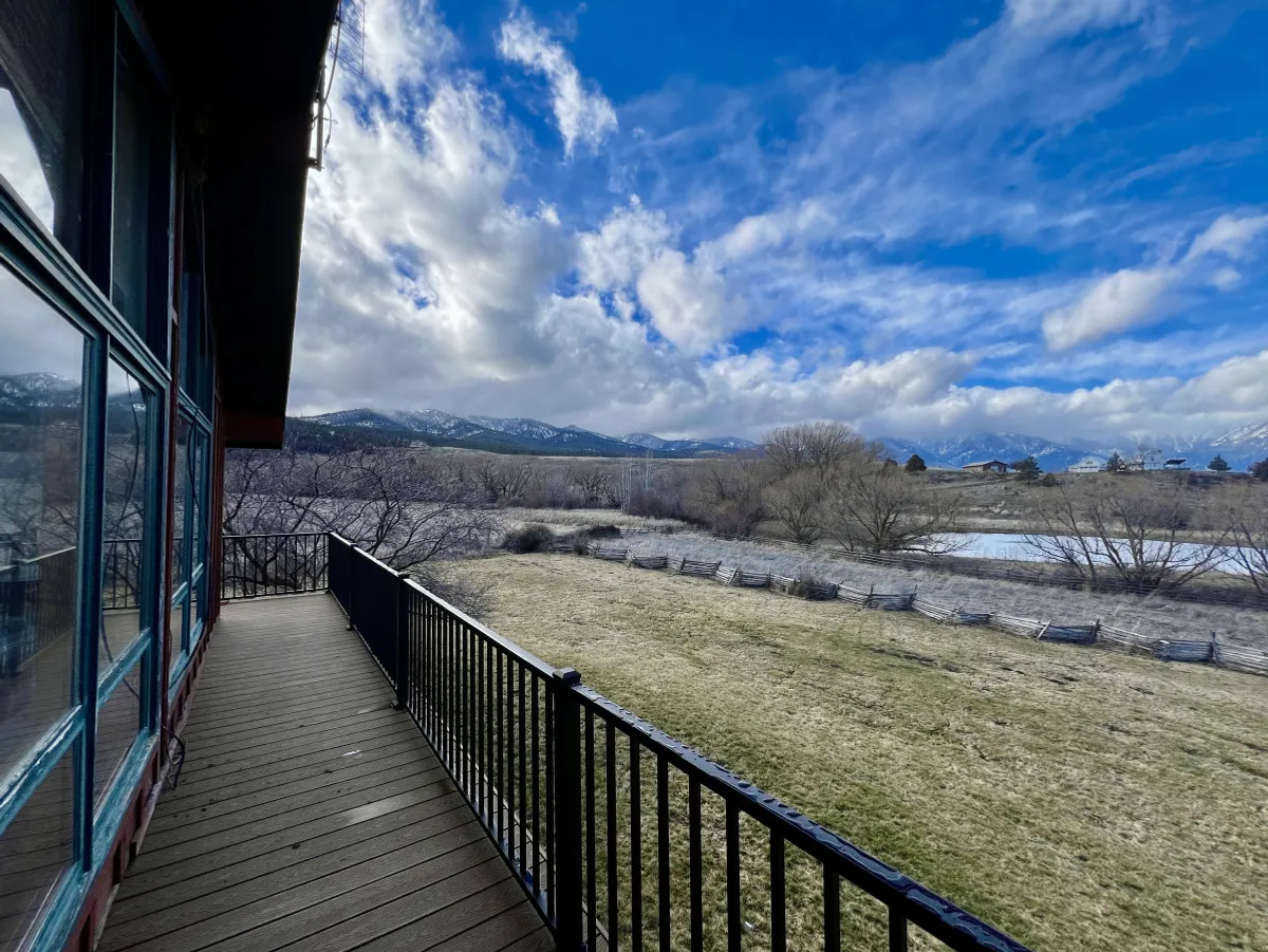 A sweeping view of a majestic mountain range, a winding river, and an open grassy field under a dramatic cloudy sky. The natural landscape evokes a sense of possibility for outdoor activities like hiking, bird watching, and simply soaking in the beauty of the Elkhorn Mountains.