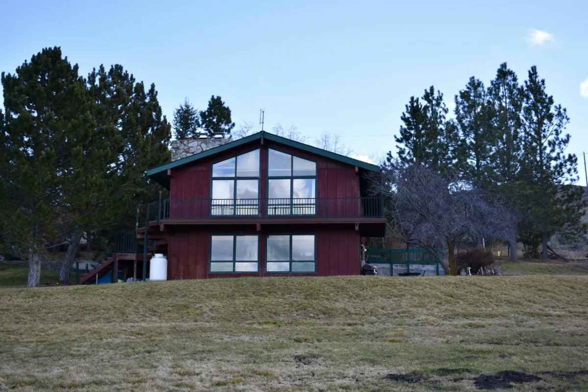 The red-sided house features large windows overlooking a spacious green lawn surrounded by trees. The setting invites relaxation and outdoor activities, with ample room for lawn games or larger group celebrations.