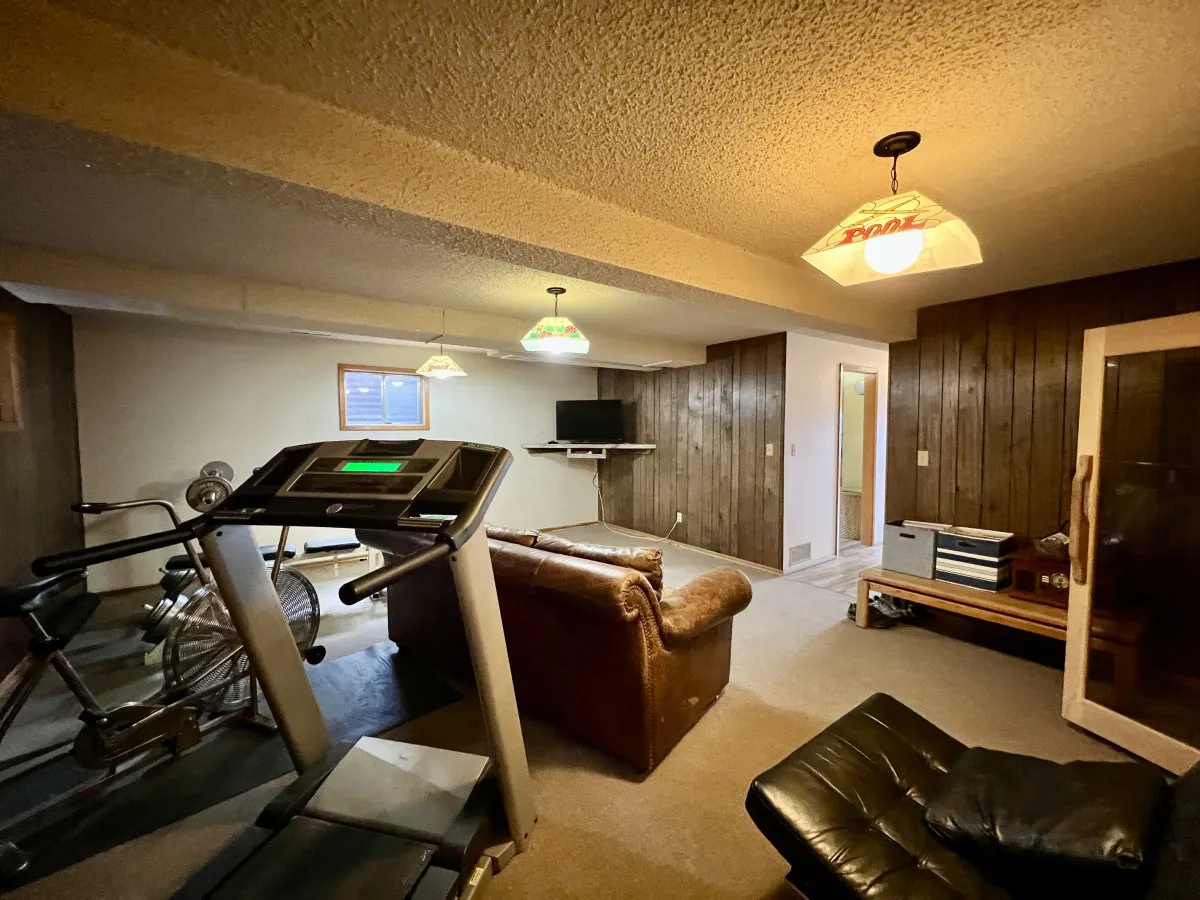 An inviting interior recreation space featuring a sauna, treadmill, cozy sofa, and television, designed for relaxation and post-adventure unwinding. The cedar sauna is highlighted, embodying the perfect retreat after a day of mountain exploration.