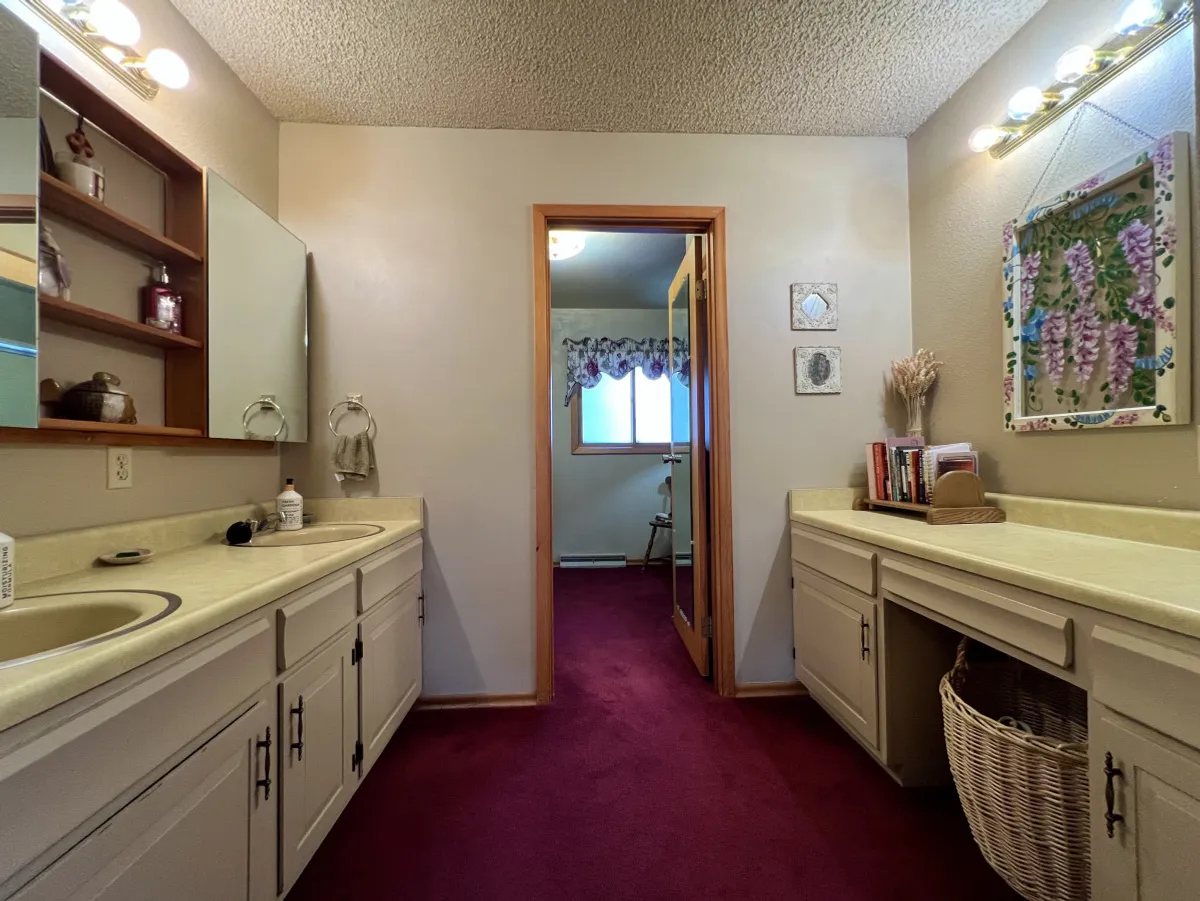 A calming bathroom space with double sink vanities, large mirrors, and soothing decorative wall art. The doorway reveals a glimpse into another peaceful room, adding a sense of spaciousness and convenience.