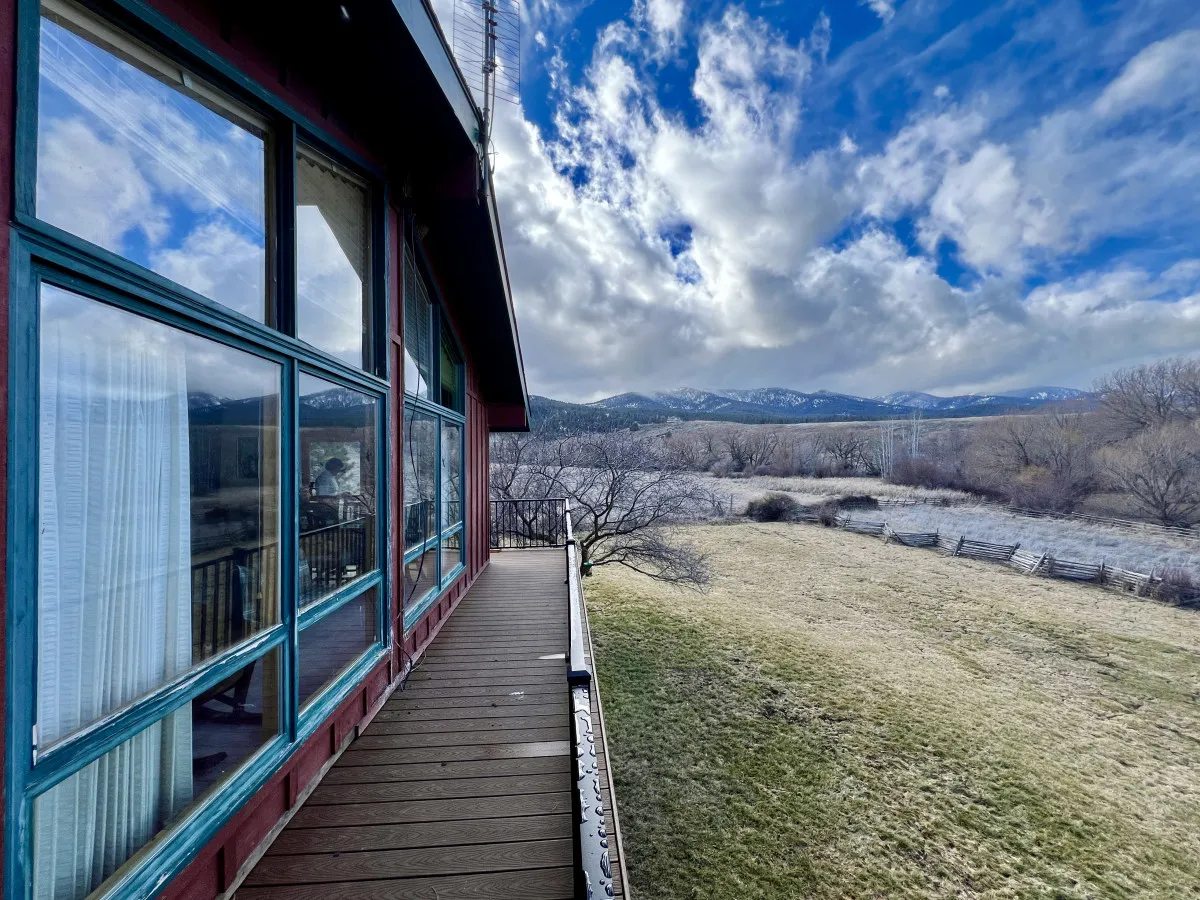 A panoramic view of the mountains serves as a backdrop to a spacious balcony and lush green grass below. The perspective captures the inviting outdoor environment and the ample lawn space available for events or relaxation.