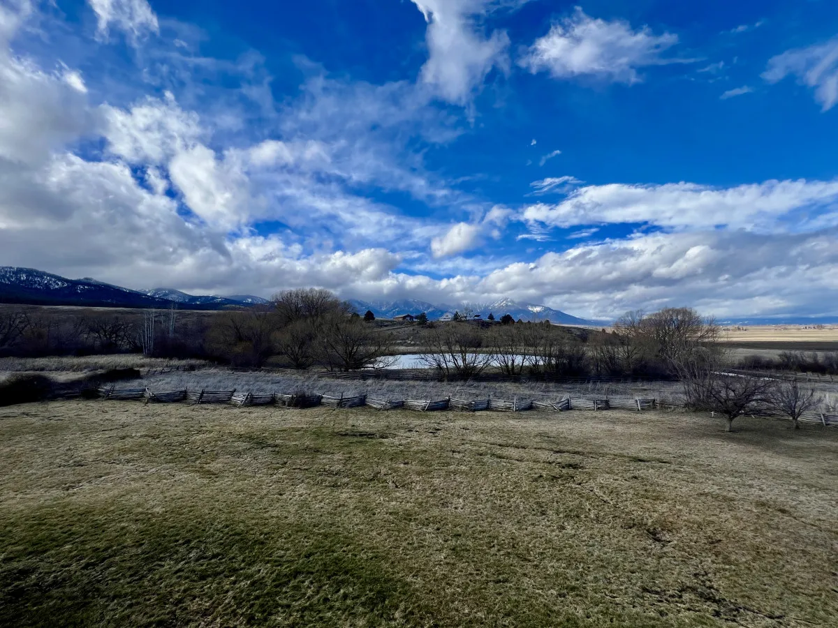 A sweeping landscape view featuring distant mountains, calm water, open fields, and a cloudy sky. The scene evokes a sense of openness and connection to nature—ideal for outdoor breaks, reflection, or post-work exploration.